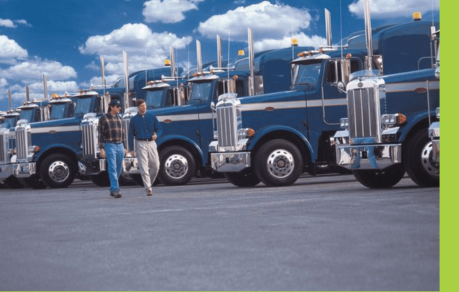 A row of large trucks parked in front of a man.